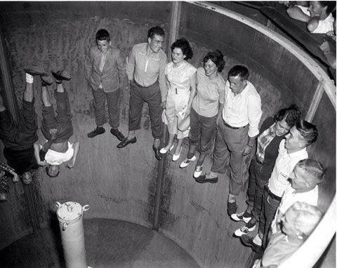 black and white photograph of people standing in a round room looking up at the sky