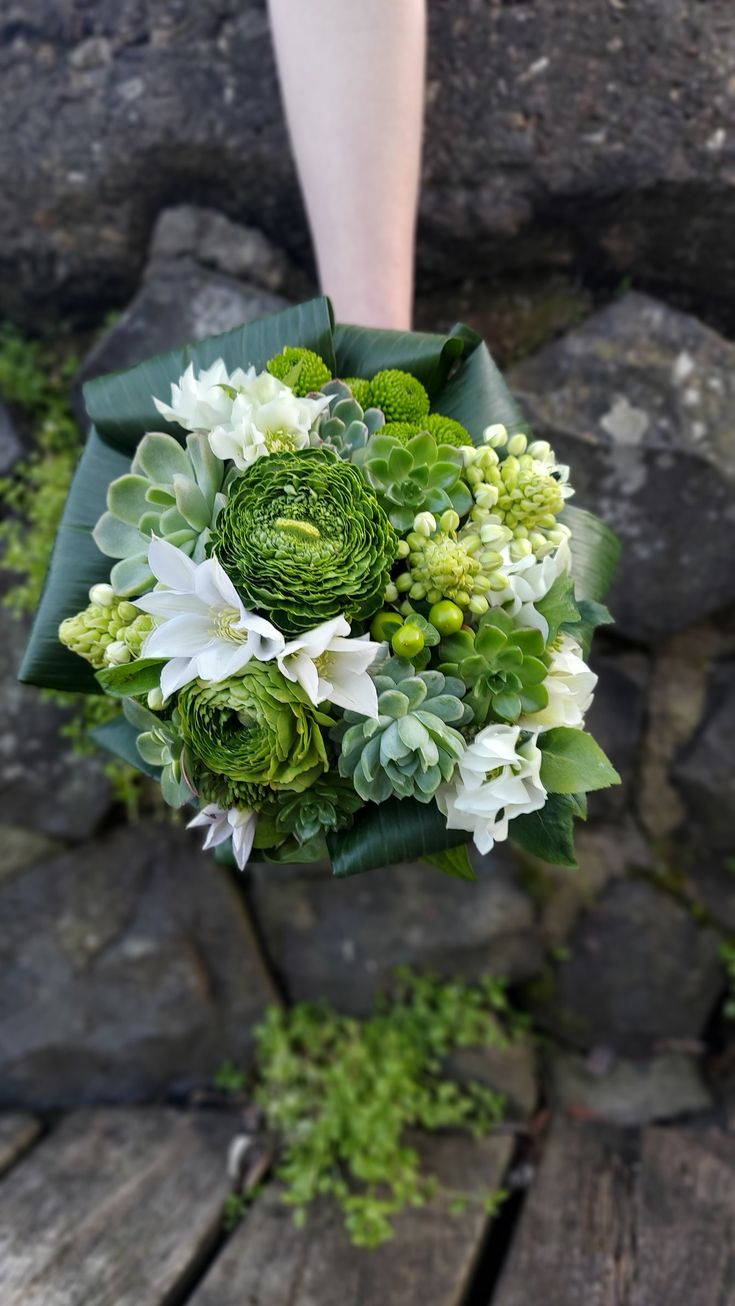 a bride's bouquet with white and green flowers on a wooden table next to rocks