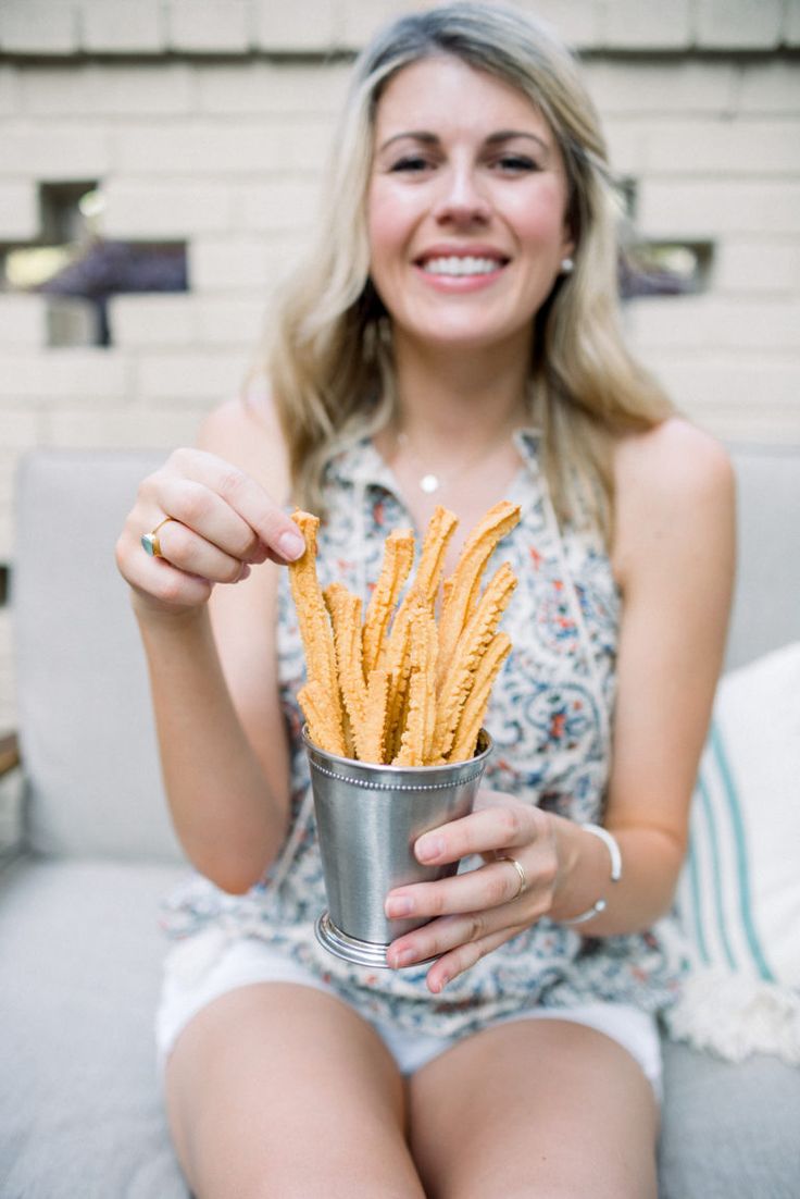 a woman sitting on a couch holding a cup filled with fries