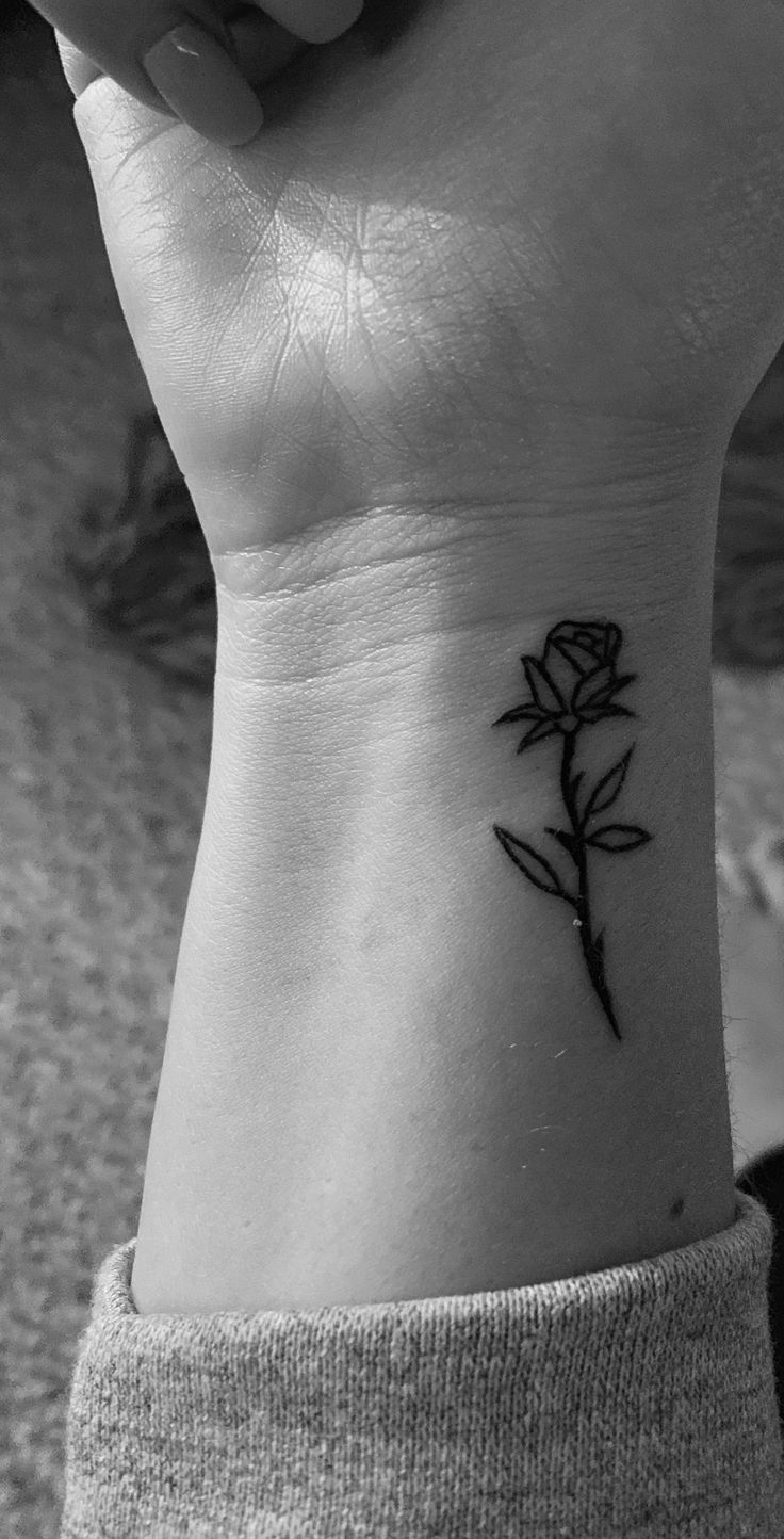 a black and white photo of a woman's wrist with a rose tattoo on it