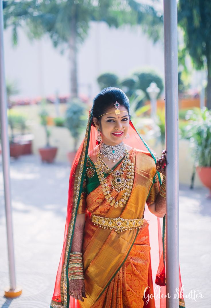 a woman in an orange and green sari with jewelry on her neck, standing outside