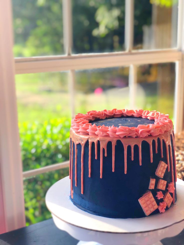 a blue and pink cake with icing on it sitting in front of a window