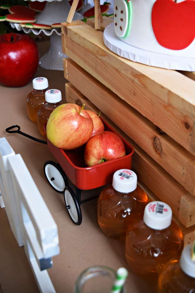 apples in a red wagon next to bottles of apple cider and an apple juicer