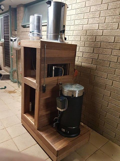 a coffee maker sitting on top of a wooden stand in front of a brick wall