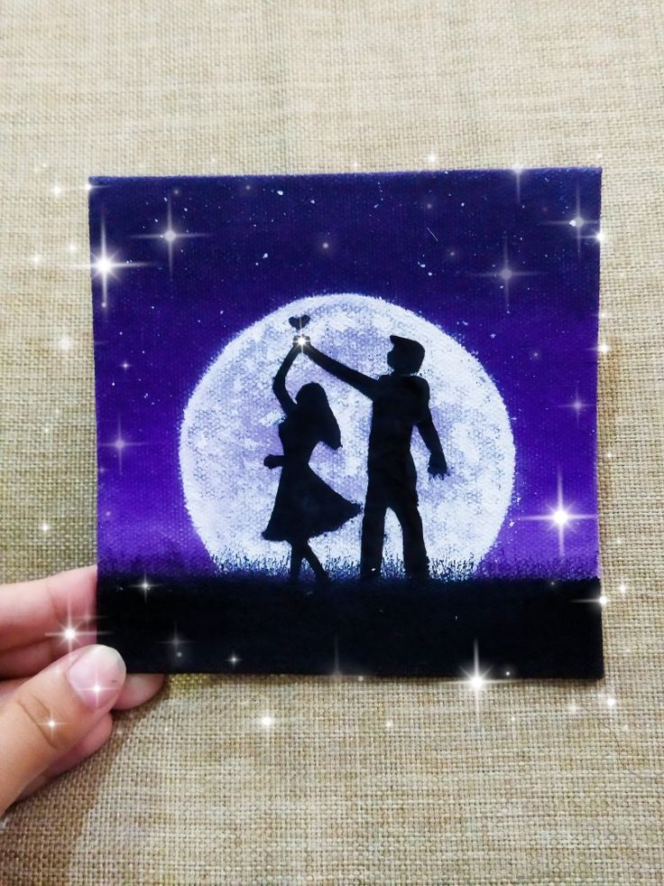 a hand holding up a card with the silhouette of a man and woman dancing in front of a full moon