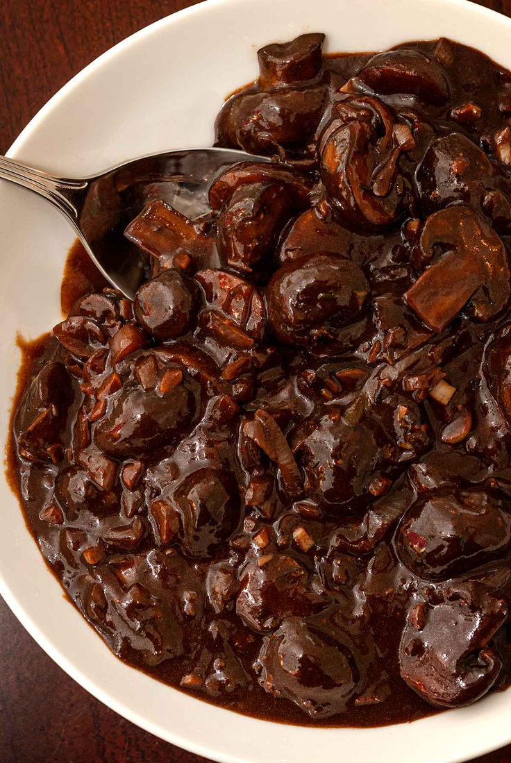 a white bowl filled with chocolate covered raisins and sauce on top of a wooden table