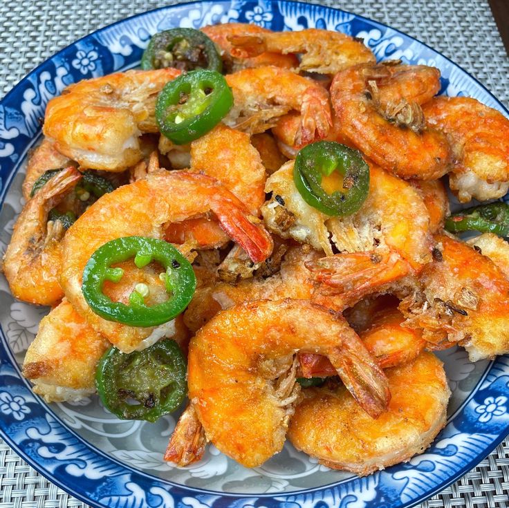 a blue and white plate filled with shrimp, peppers and jalapenos on top of a table