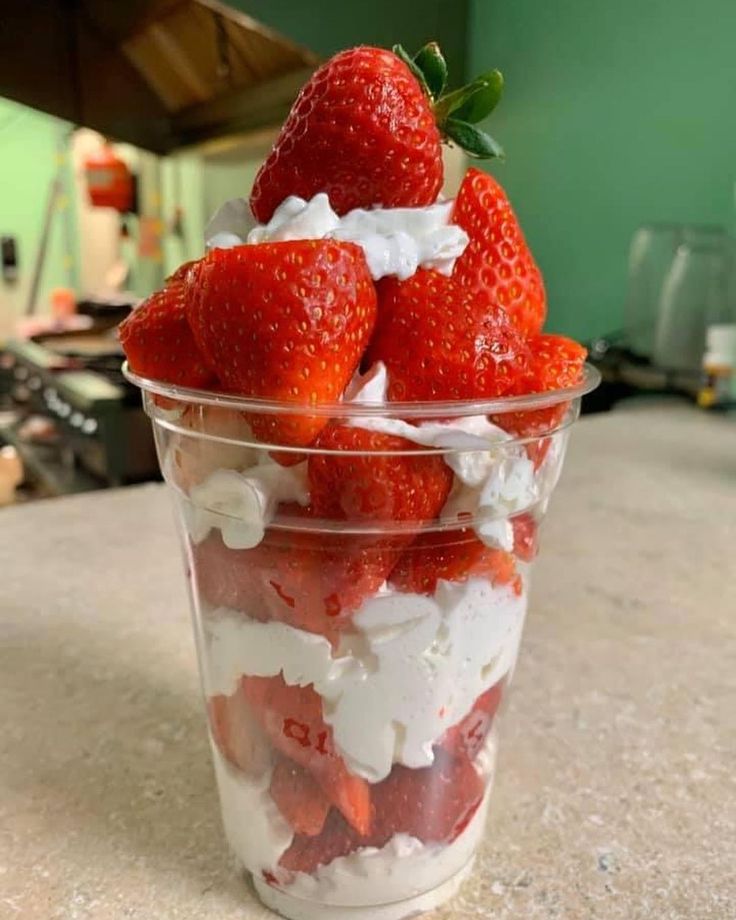 strawberries and whipped cream in a plastic cup on a counter top with other food items