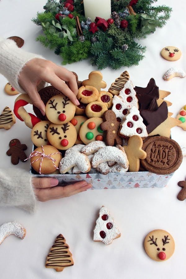 a person holding a box filled with cookies and other holiday treats on top of a table