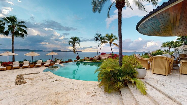 an outdoor swimming pool with lounge chairs and umbrellas next to the water, surrounded by palm trees