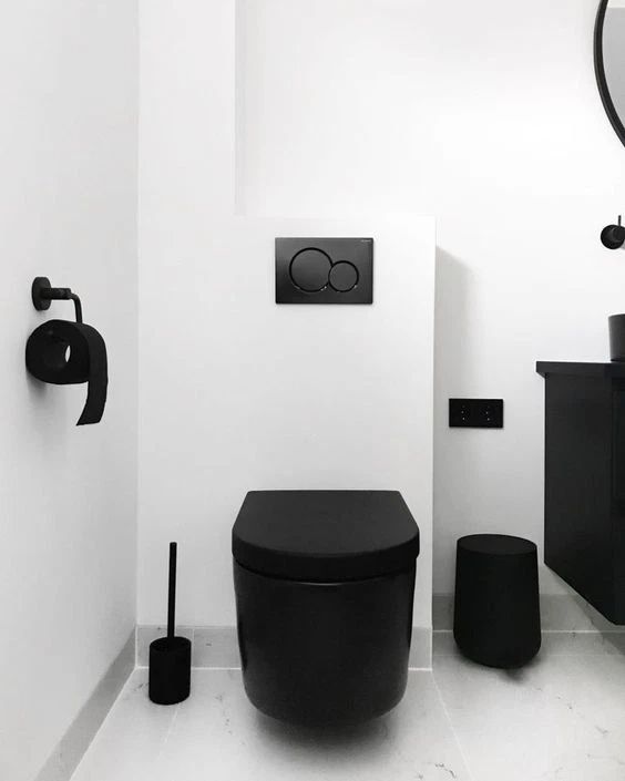 a black toilet sitting next to a sink in a white bathroom with an odd shaped faucet