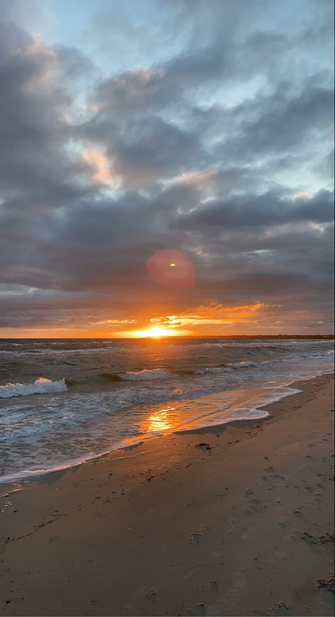 the sun is setting over the ocean with clouds in the sky and waves on the beach