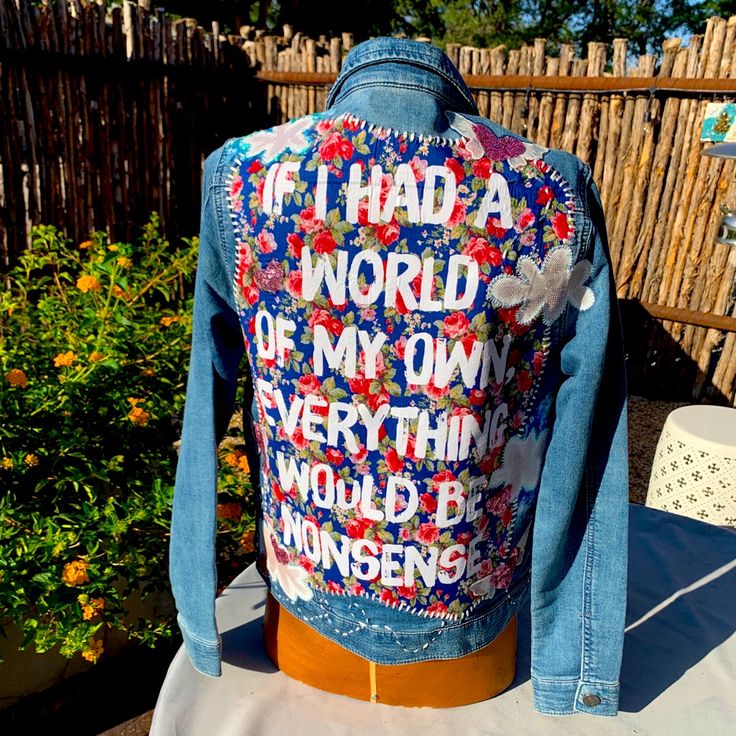 a denim jacket with words on it sitting on a table in front of a fence