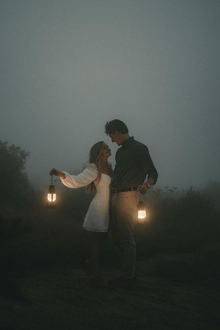 a man and woman standing in the fog holding two lanterns with their arms around each other