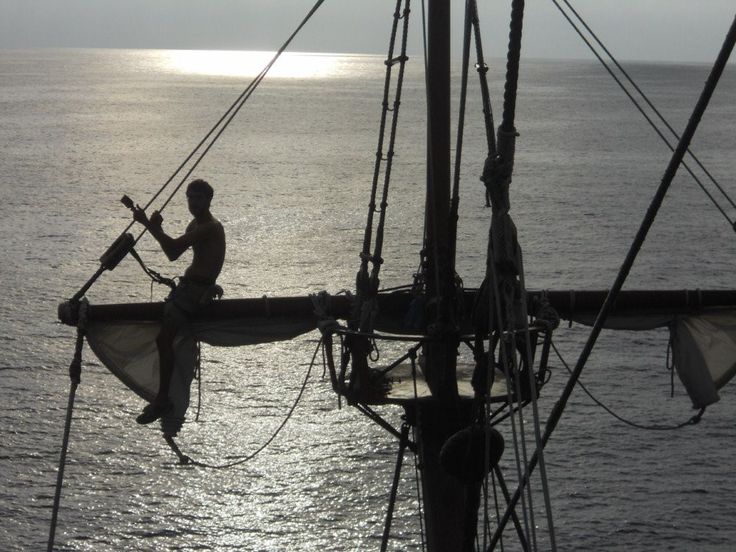 a man sitting on top of a sail boat in the middle of the ocean at sunset