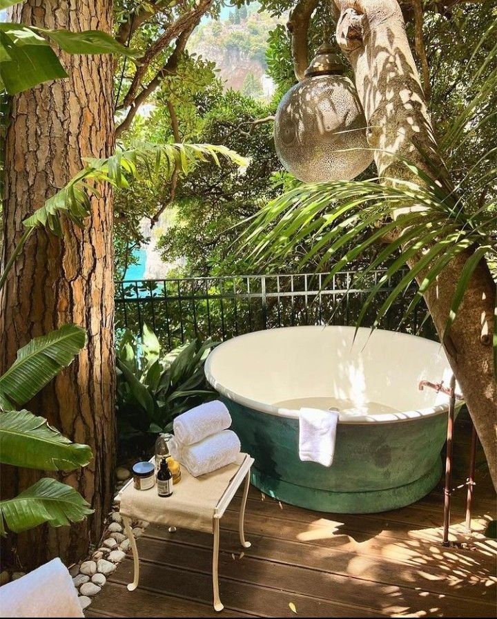 an outdoor bathtub in the middle of a tree lined deck with towels on it