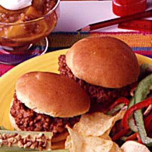 two sloppy joe sandwiches on a yellow plate with chips and pickle wedges next to it