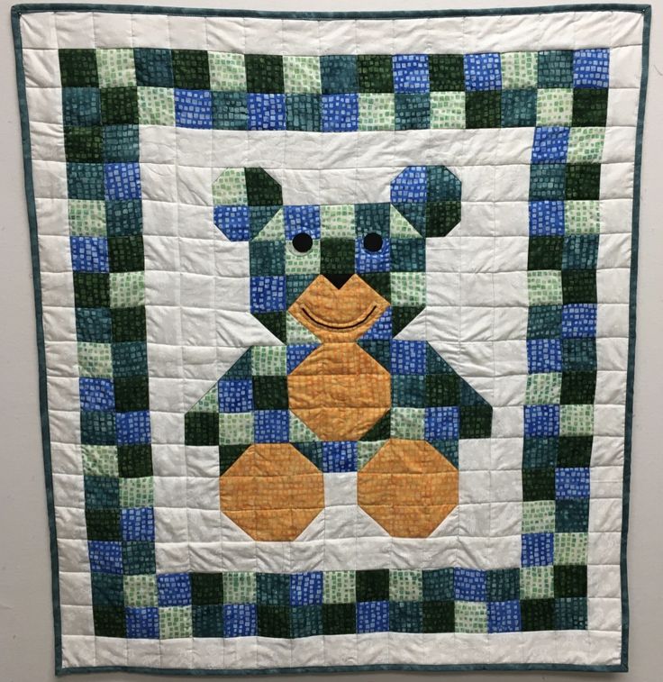 a blue and green teddy bear quilted onto a wall hanging on a white wall