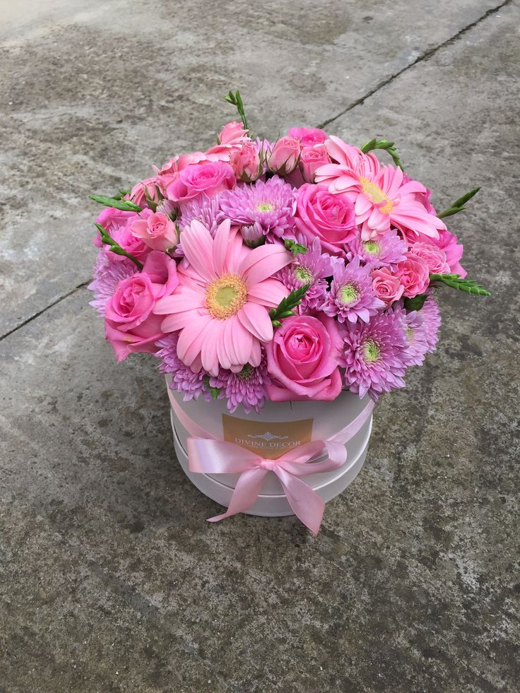 a bouquet of pink flowers in a round box on the ground with a ribbon around it