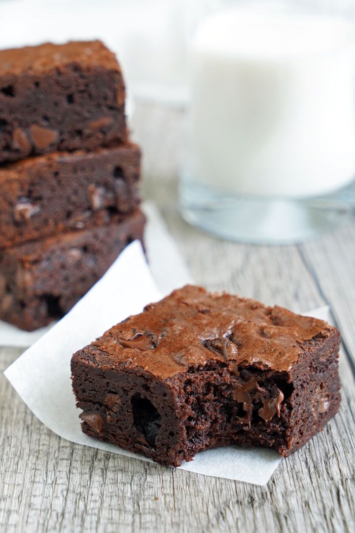 two pieces of brownie sitting on top of white napkins next to a glass of milk