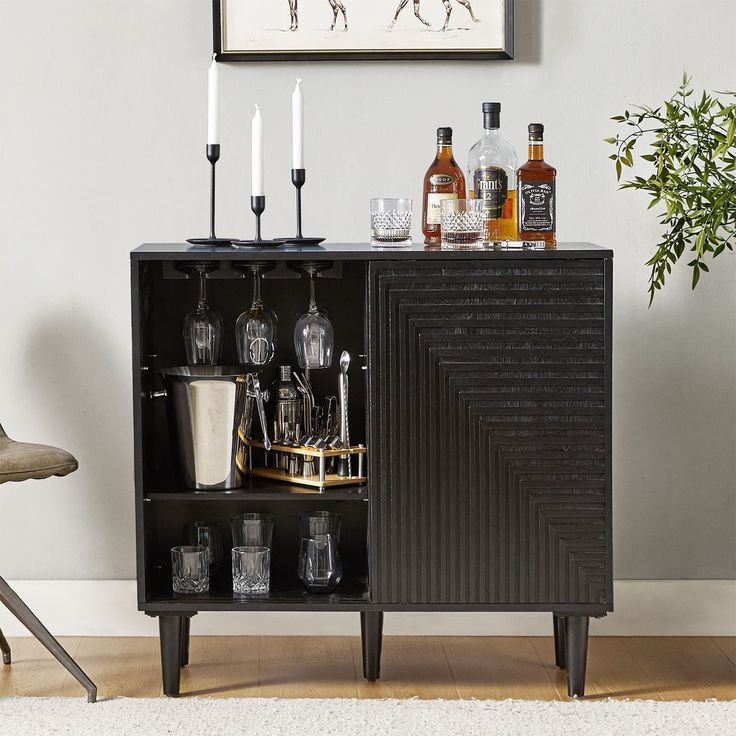 a black cabinet with liquor bottles and glasses on it in front of a framed picture