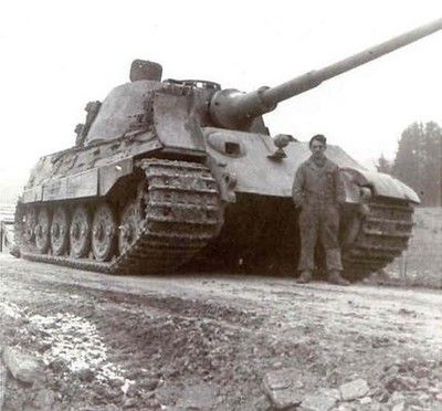 two men standing next to a tank on the side of a road in front of some rocks