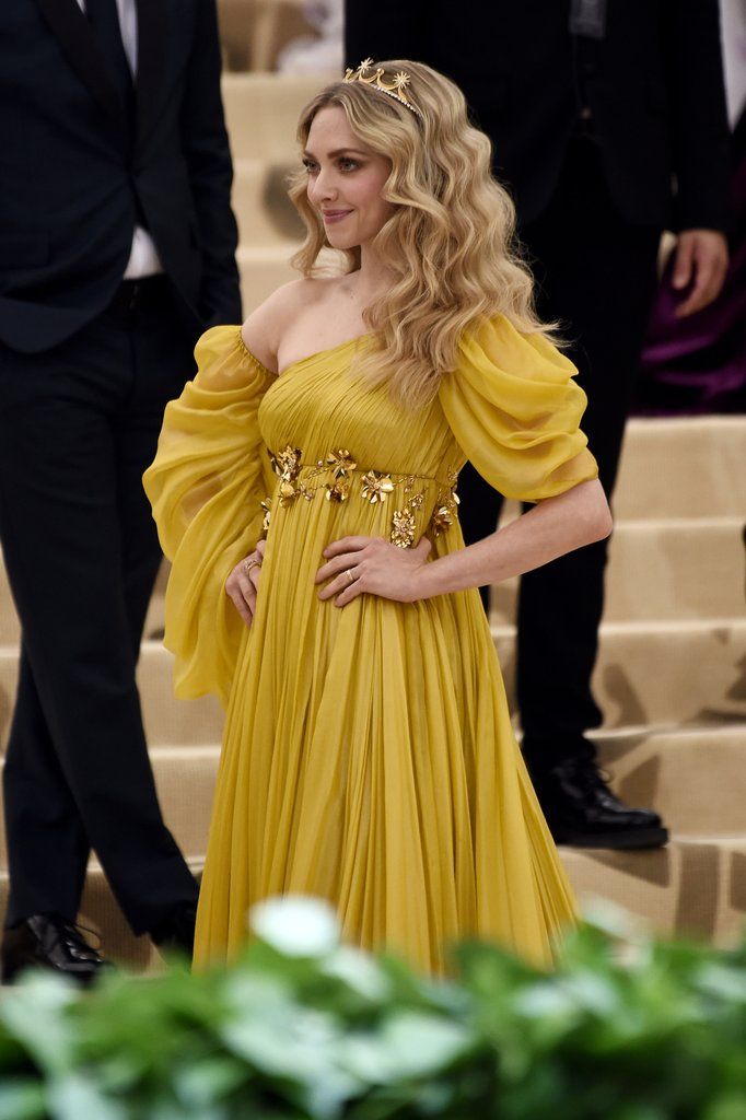 a woman in a yellow dress standing next to some stairs with other people behind her