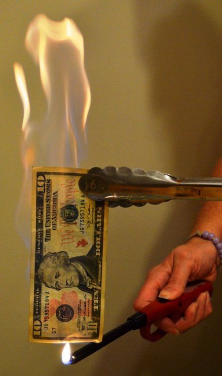 a person holding a pair of scissors over a burning dollar bill