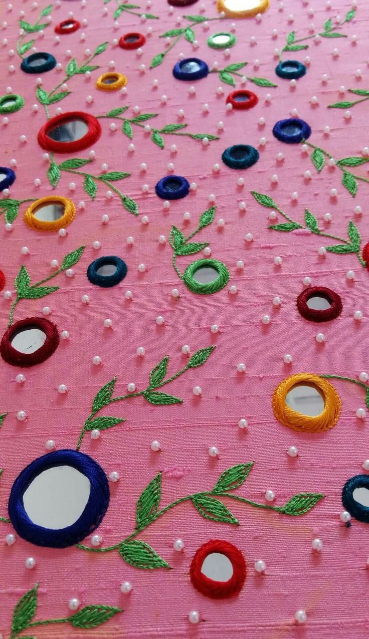 a pink table cloth with various colored circles and leaves on it, along with beads