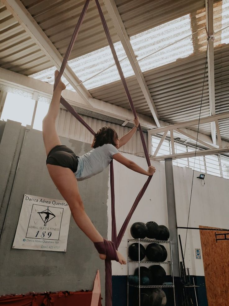 a woman is performing aerial acrobatics on a pole in an indoor gym