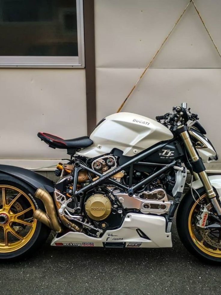 a white and gold motorcycle parked in front of a building next to a wall with windows