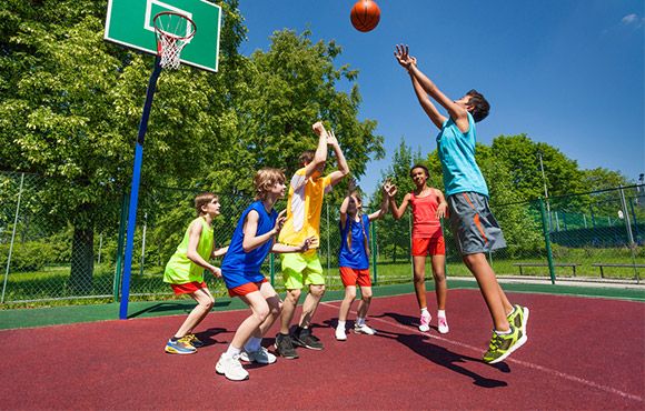 a group of young people playing basketball on an outdoor court with trees in the background