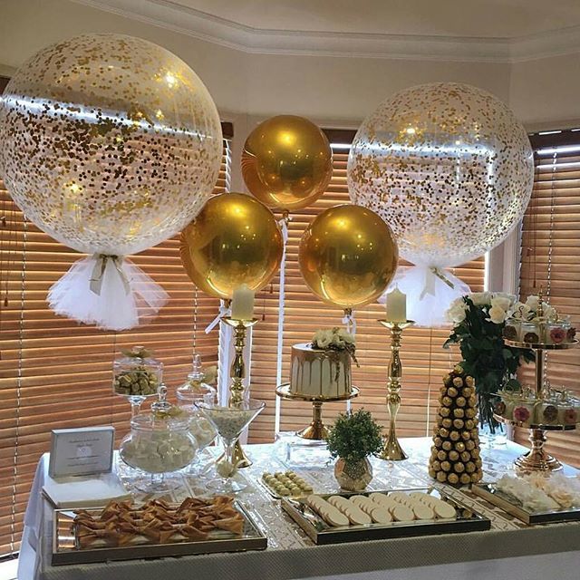 a table topped with lots of balloons filled with gold and white confetti balls