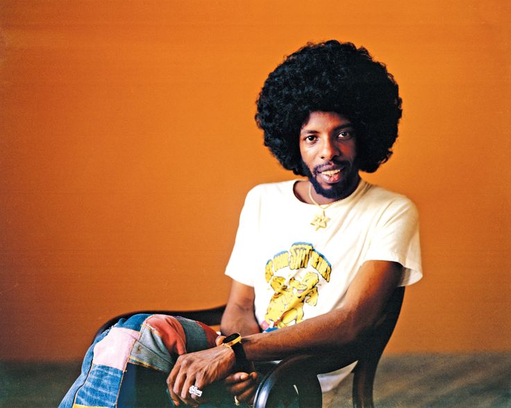 a man sitting in a chair with an afro on his head and wearing a white t - shirt