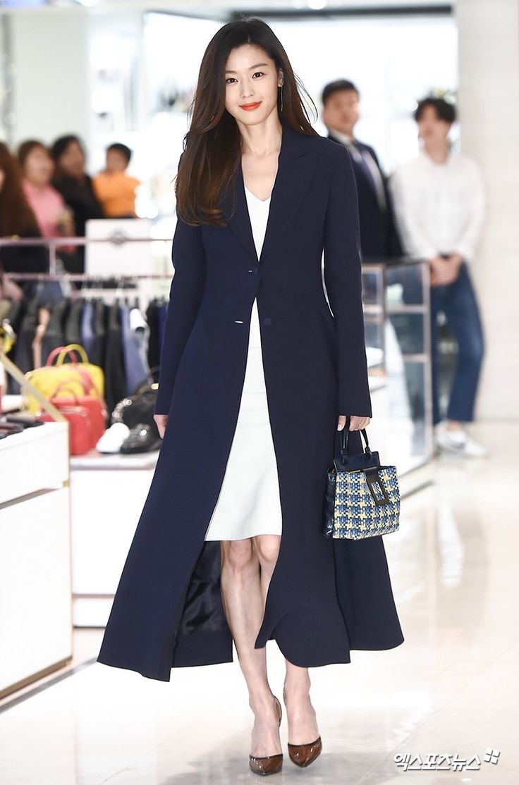 a woman is walking down the runway in a blue coat and white dress with black heels