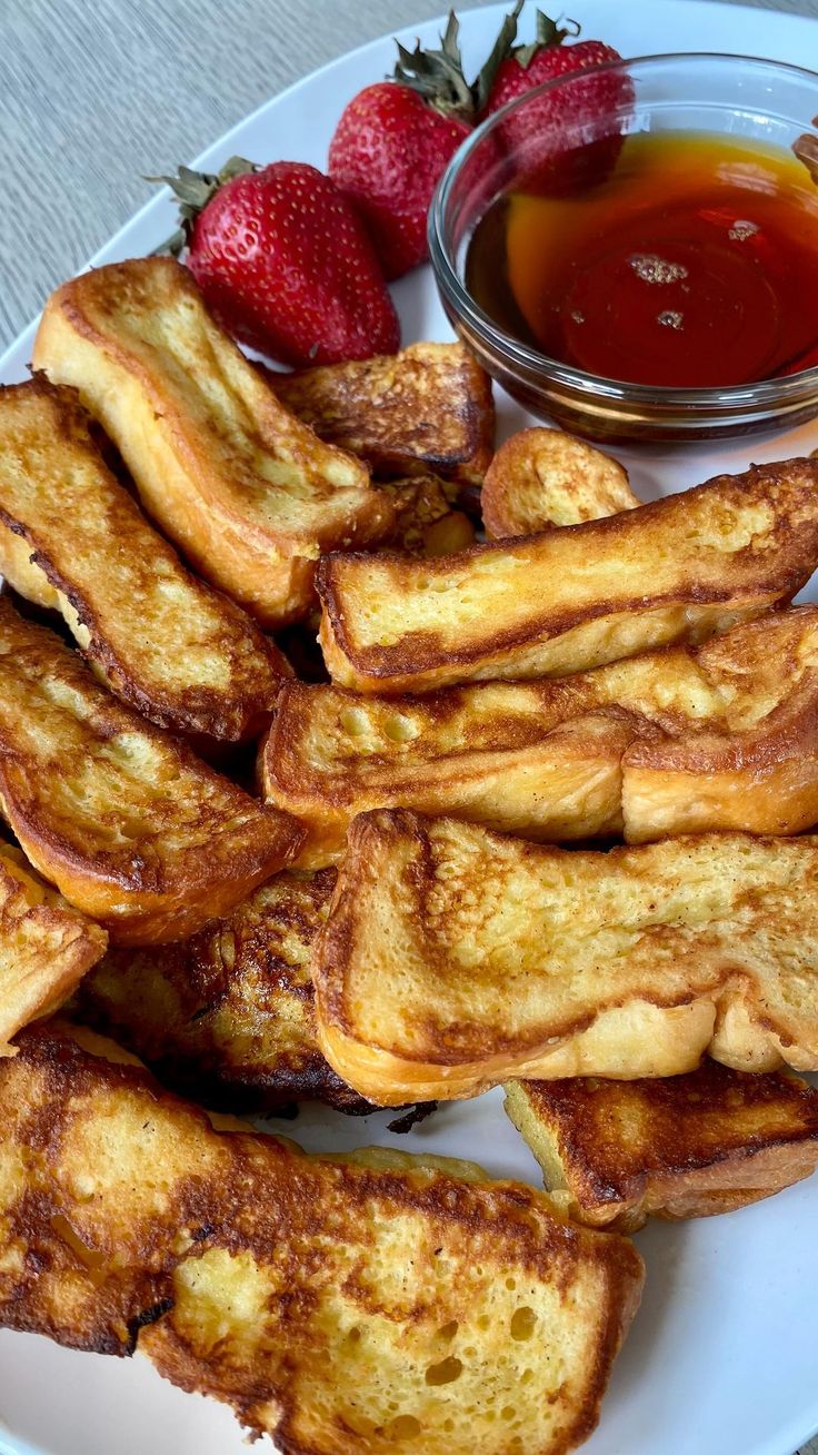 some french toast on a white plate with strawberries and ketchup in a bowl