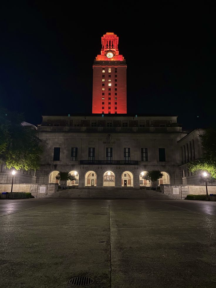 a large building with a clock tower lit up in the dark night time at its entrance