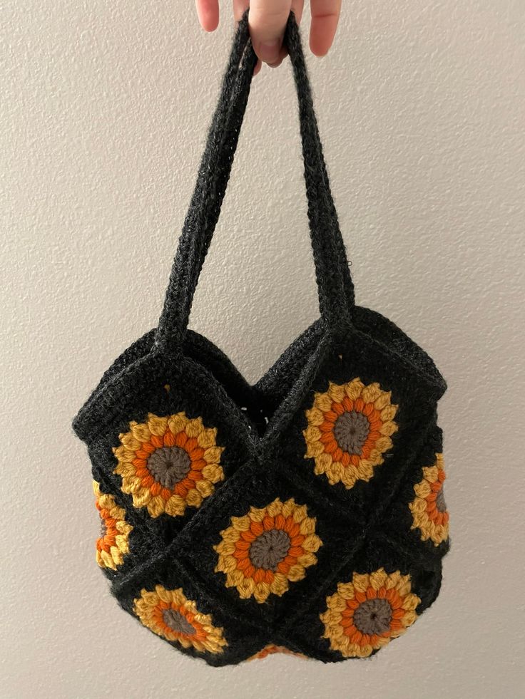 a crocheted sunflower purse hanging from a hook on a wall with a hand holding it