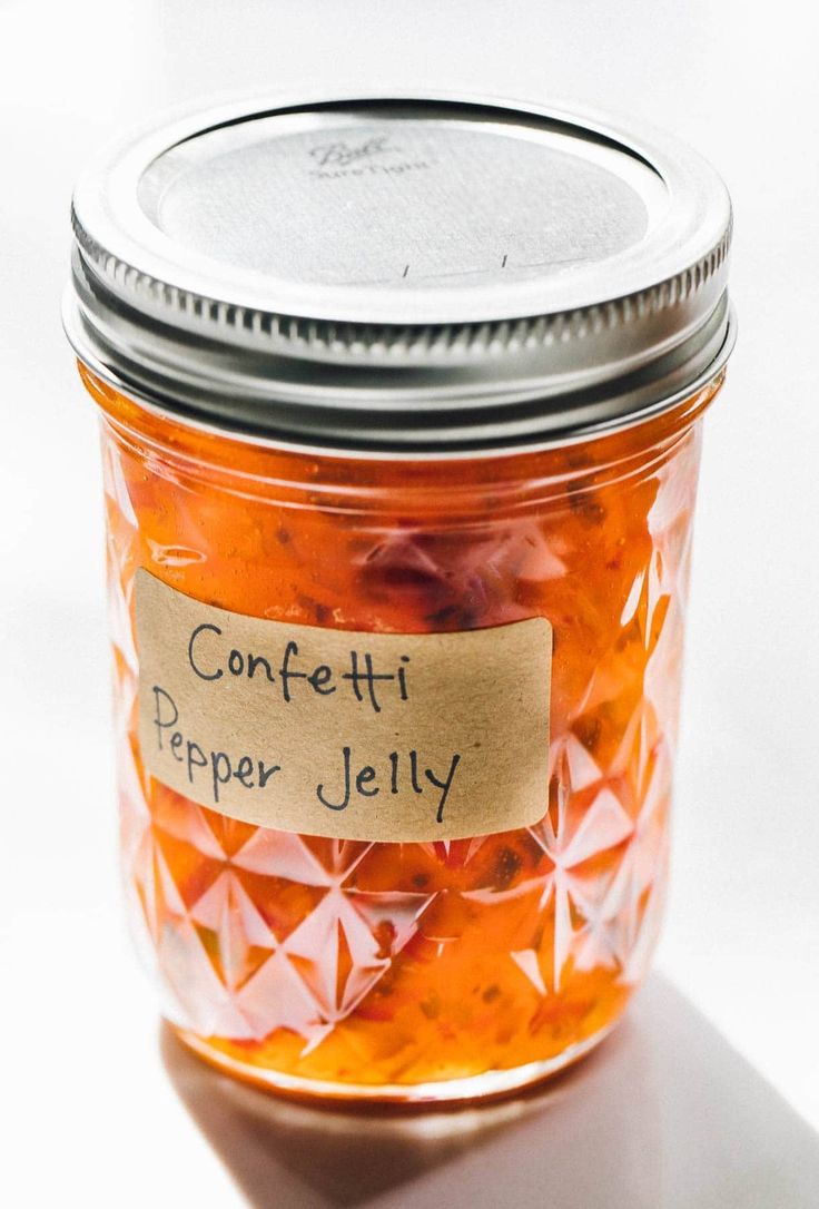 a jar filled with confetti pepper jelly sitting on top of a white table