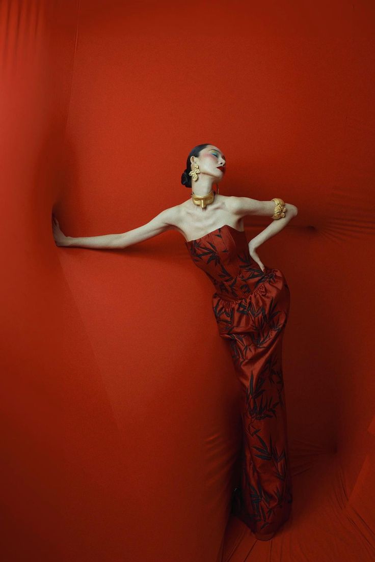 a woman in a red dress leaning against a red wall with her arms out to the side