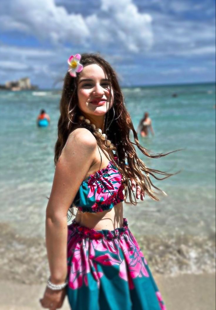 a woman standing on top of a sandy beach next to the ocean with her hair blowing in the wind