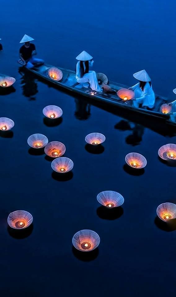 several people on a boat with paper lanterns floating in the water