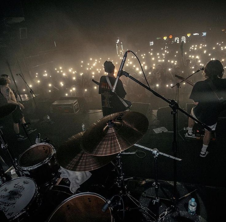 the band is playing on stage in front of an audience with their drums and microphones