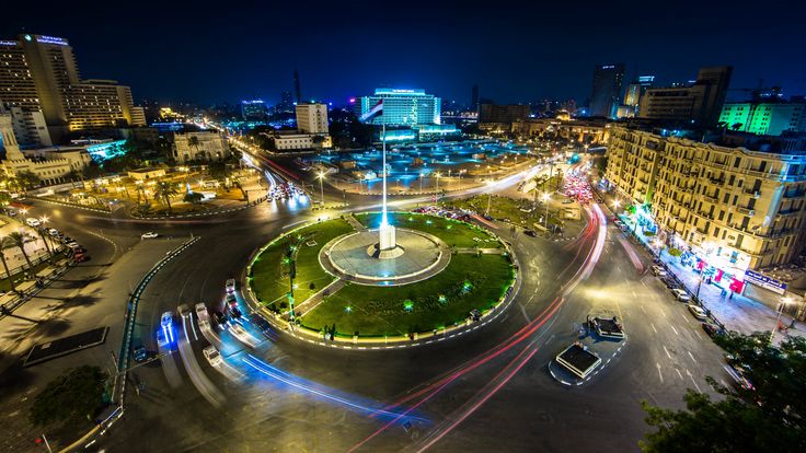 an aerial view of a city at night with traffic and lights on the streets in the foreground