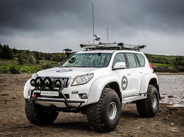 a white four wheel drive vehicle parked on the side of a body of water with dark clouds in the background