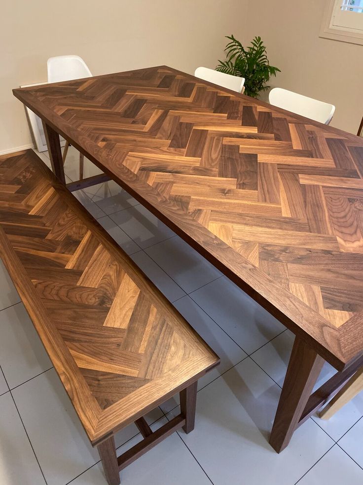 a wooden table and bench sitting on top of a tile floor next to a potted plant