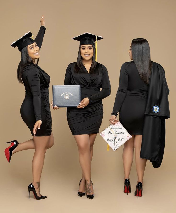 three women dressed in graduation gowns and holding laptops, posing for the camera