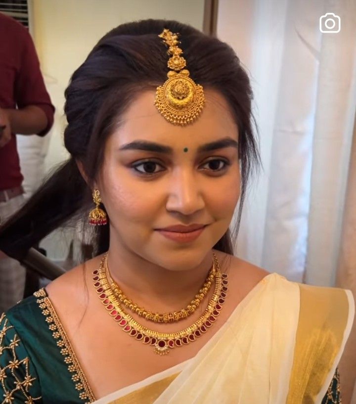 a woman in a green and gold saree with jewelry on her neck, smiling at the camera