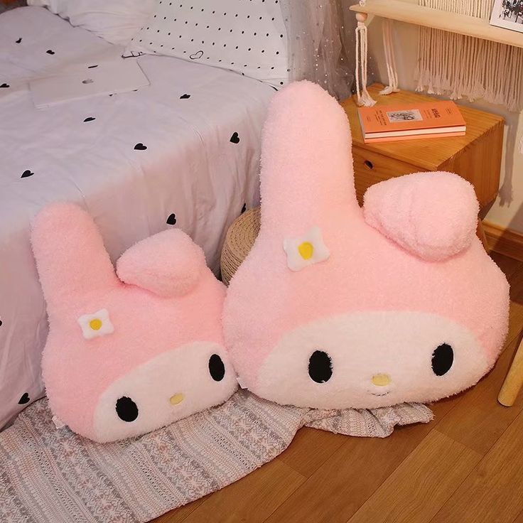 two pink hello kitty slippers sitting on top of a wooden floor next to a bed