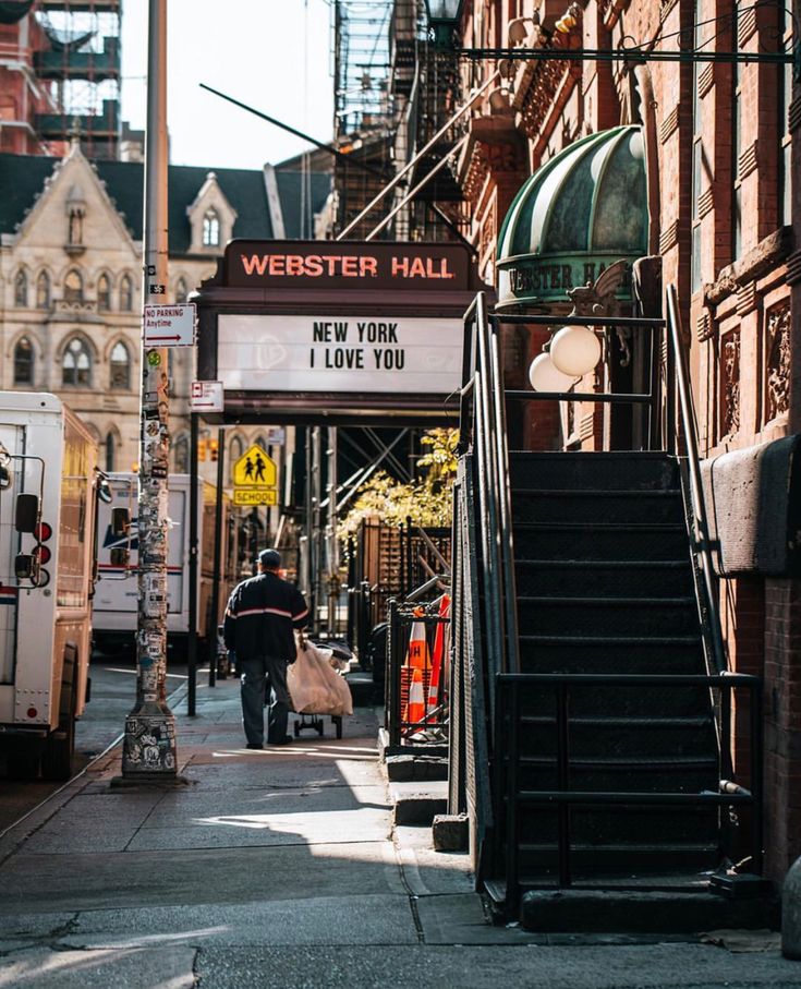 a man walking down a street next to a tall building with a sign that says webster hall